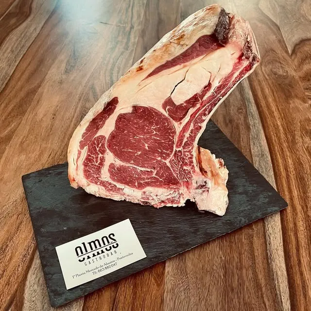 Chuletón crudo sobre tabla con la tarjeta de Olmos